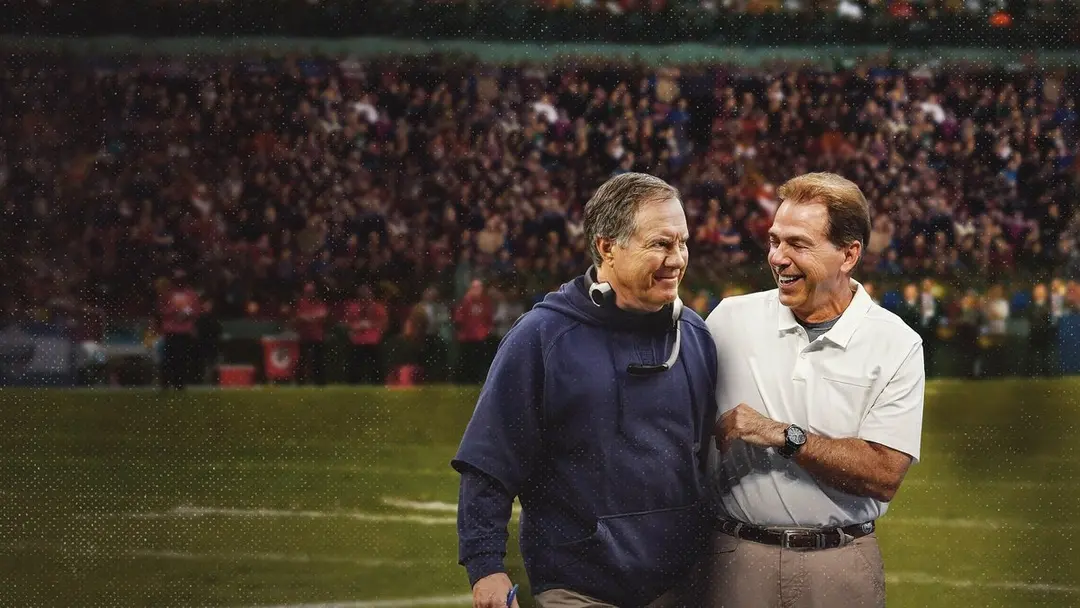 Two legendary football coaches smile together on the field.