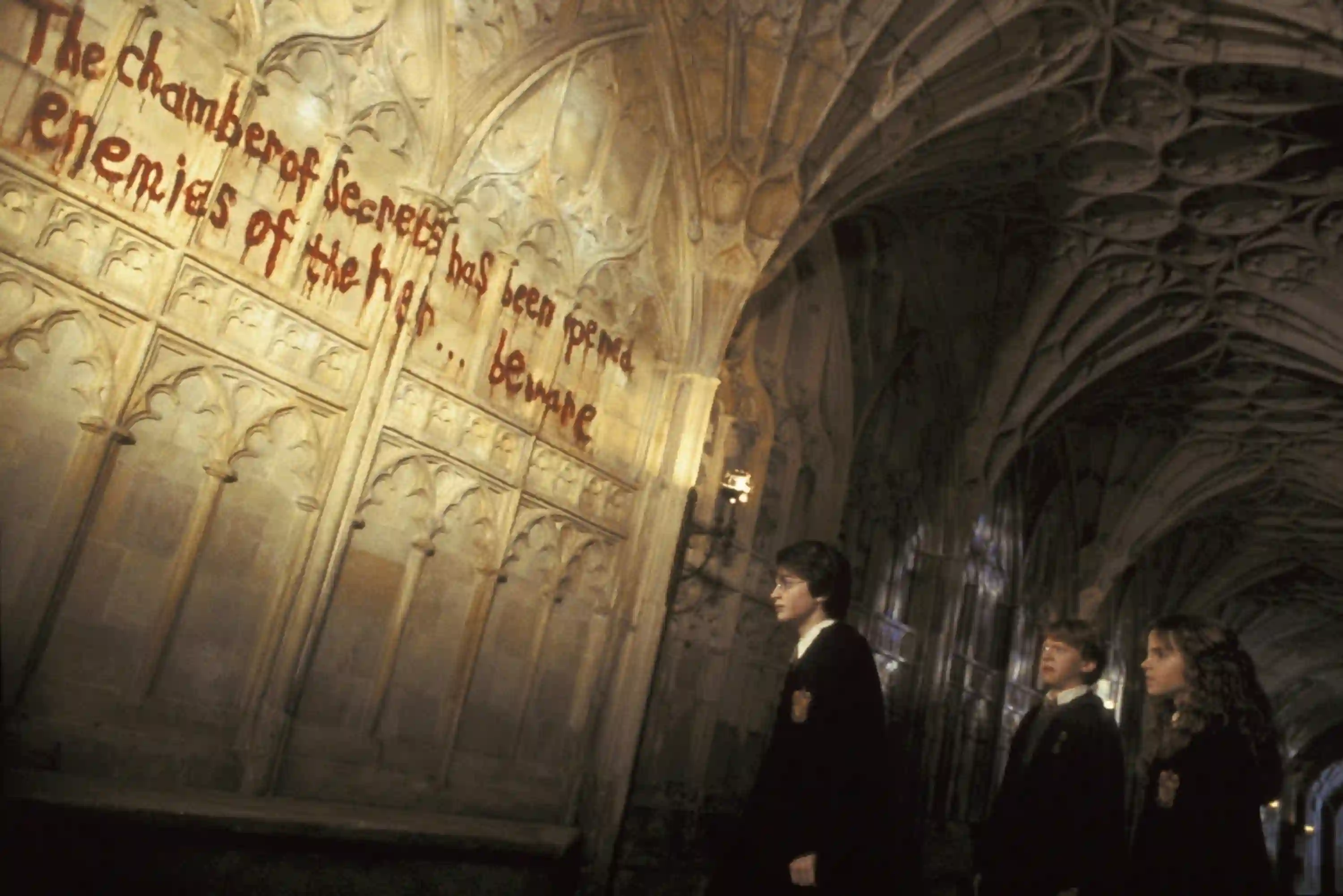 Harry, Ron, and Hermione look at words on the wall, written in blood.