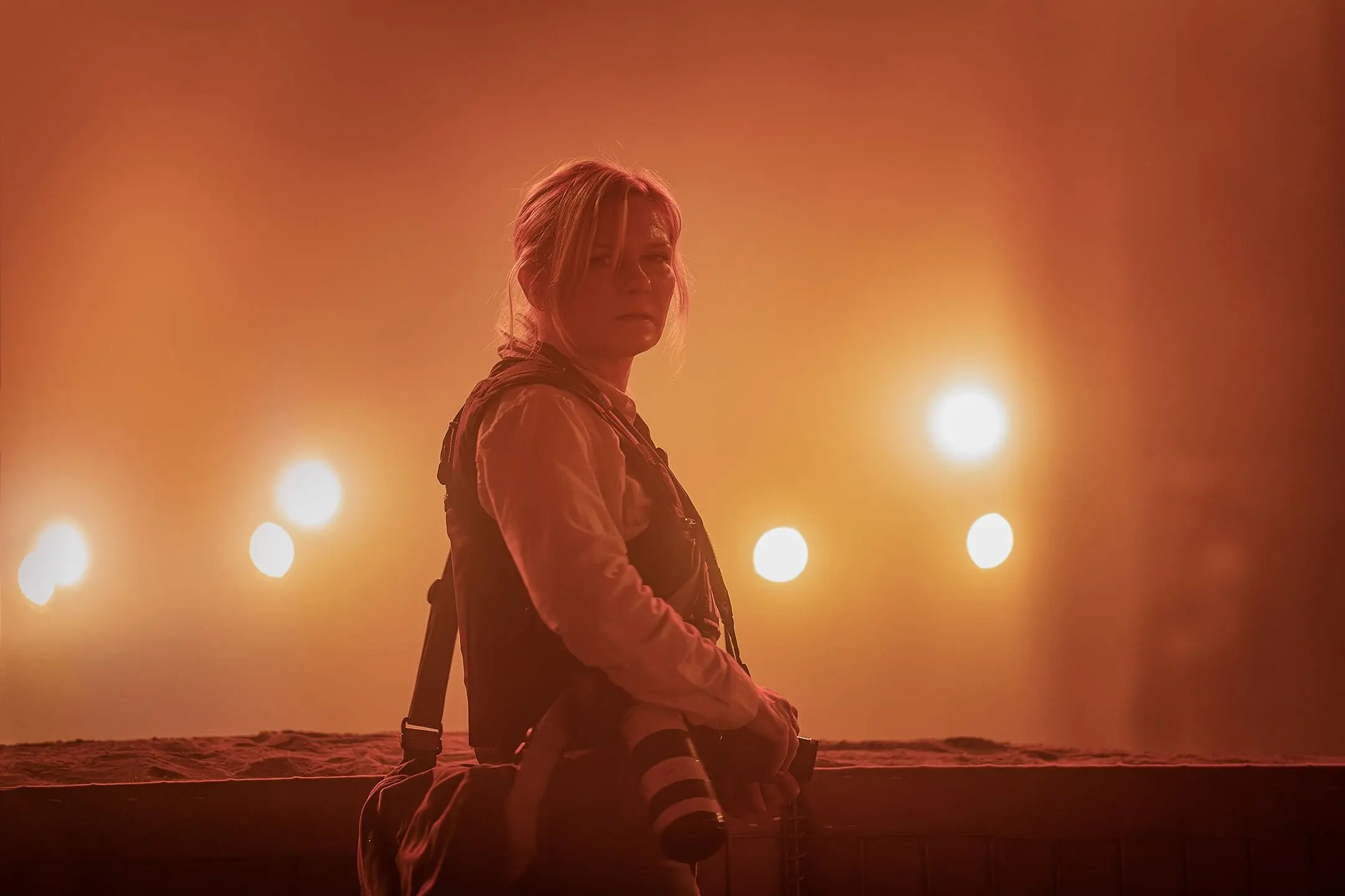 Lee (Kirsten Dunst) looks at us in the middle of a smoke-filled battlefield.