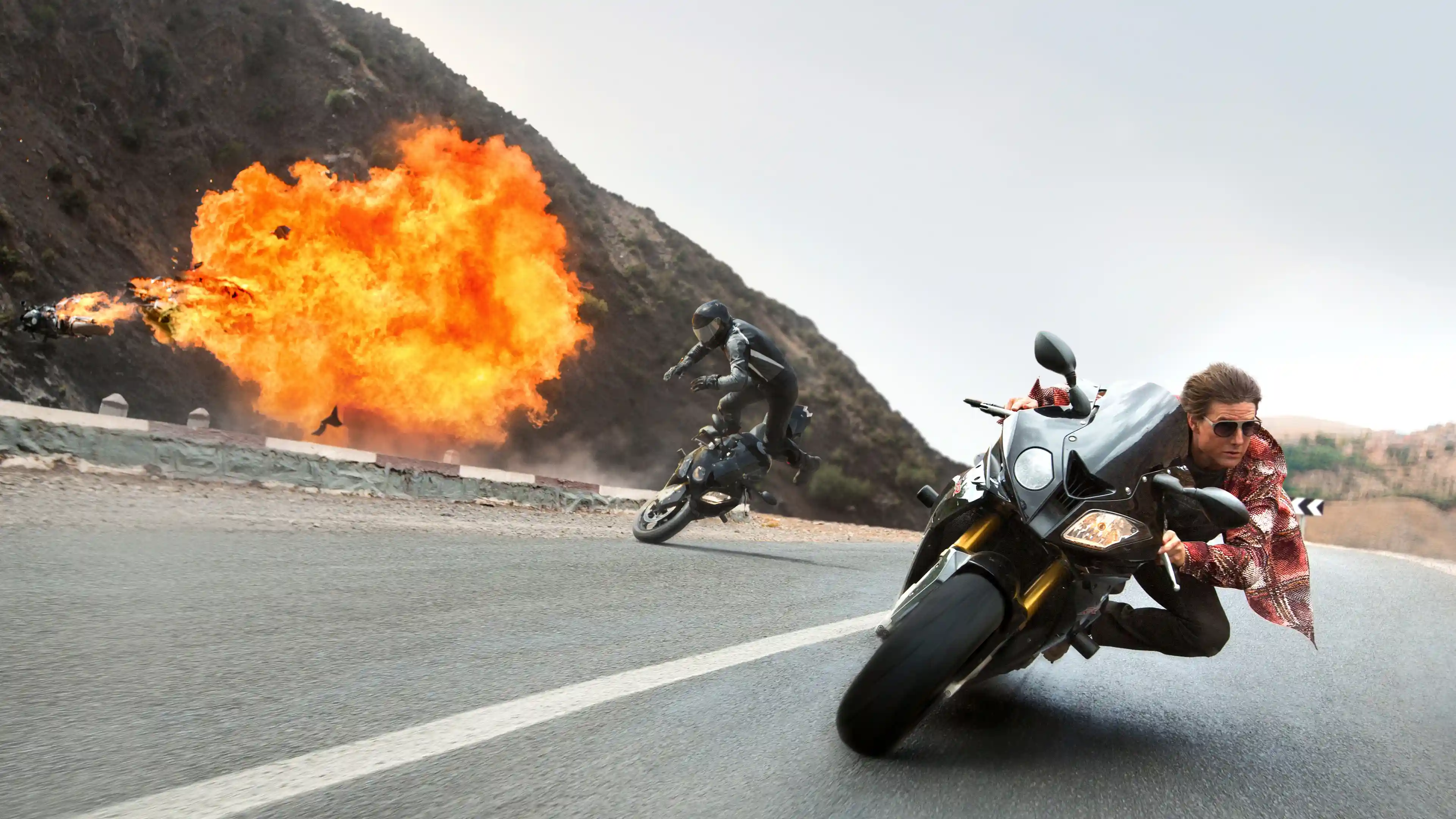 Ethan Hunt (Tom Cruise) dangerously drives his motorcycle past a crash.