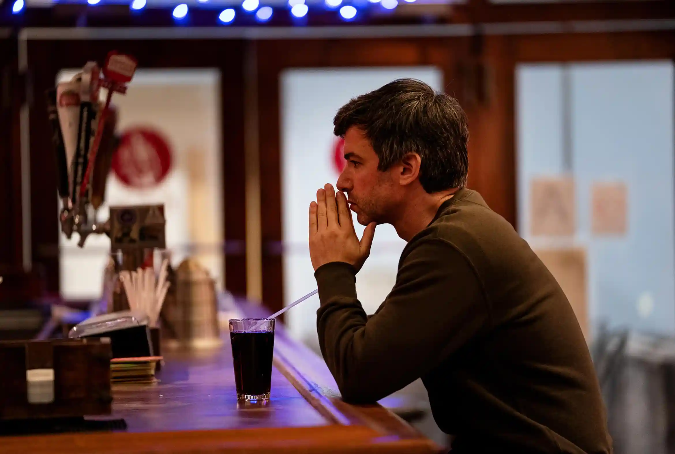 Nathan Fielder sitting at a bar with a Coke in a fictional, reality show.