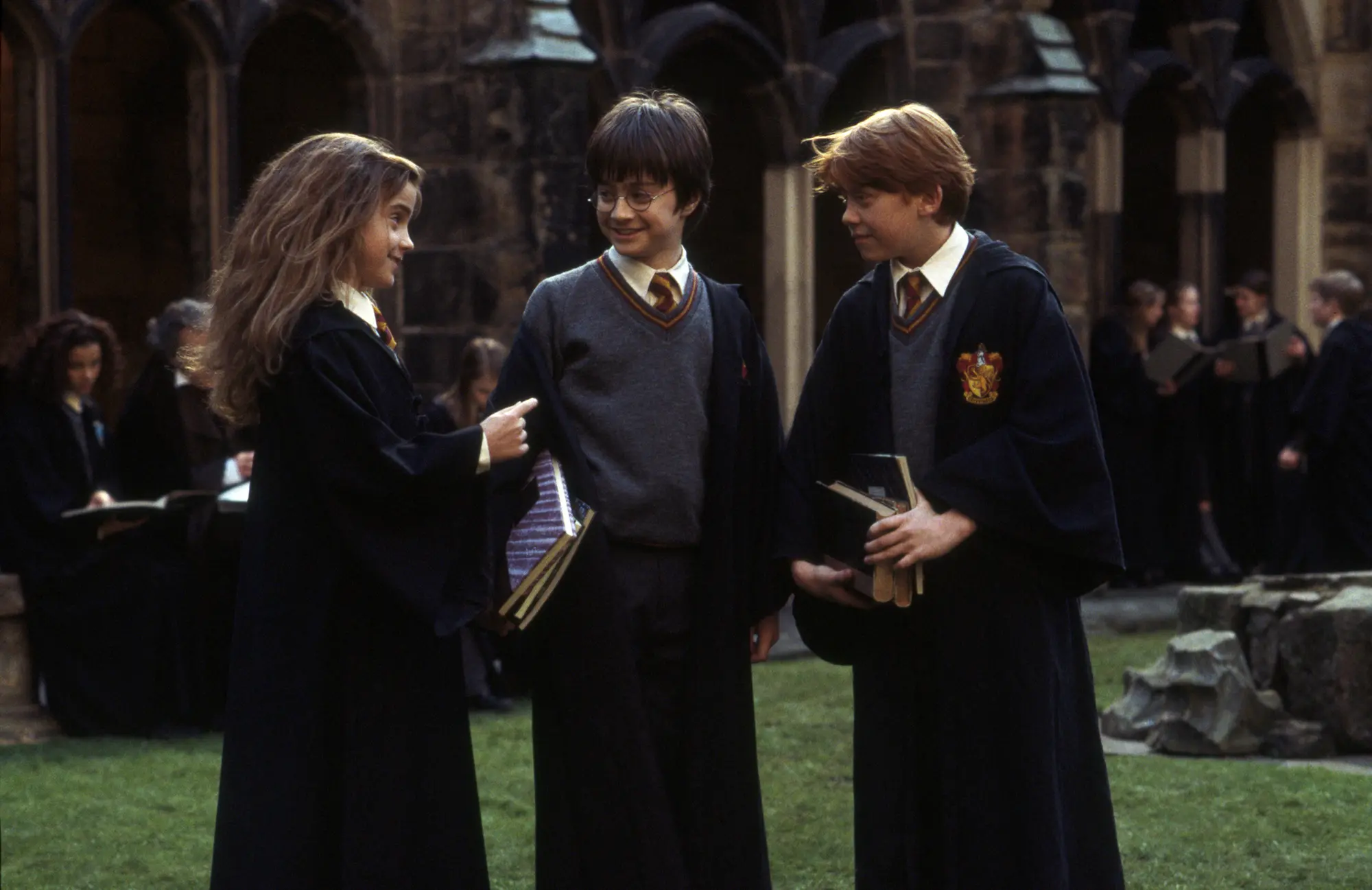 Harry, Ron, and Hermione make conversation in a Hogwarts courtyard.