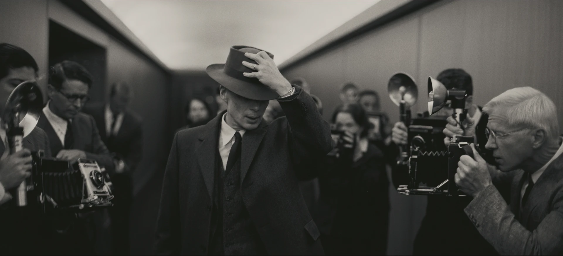 Oppenheimer (Cillian Murphy) walks down a hallway with photographers all around him.